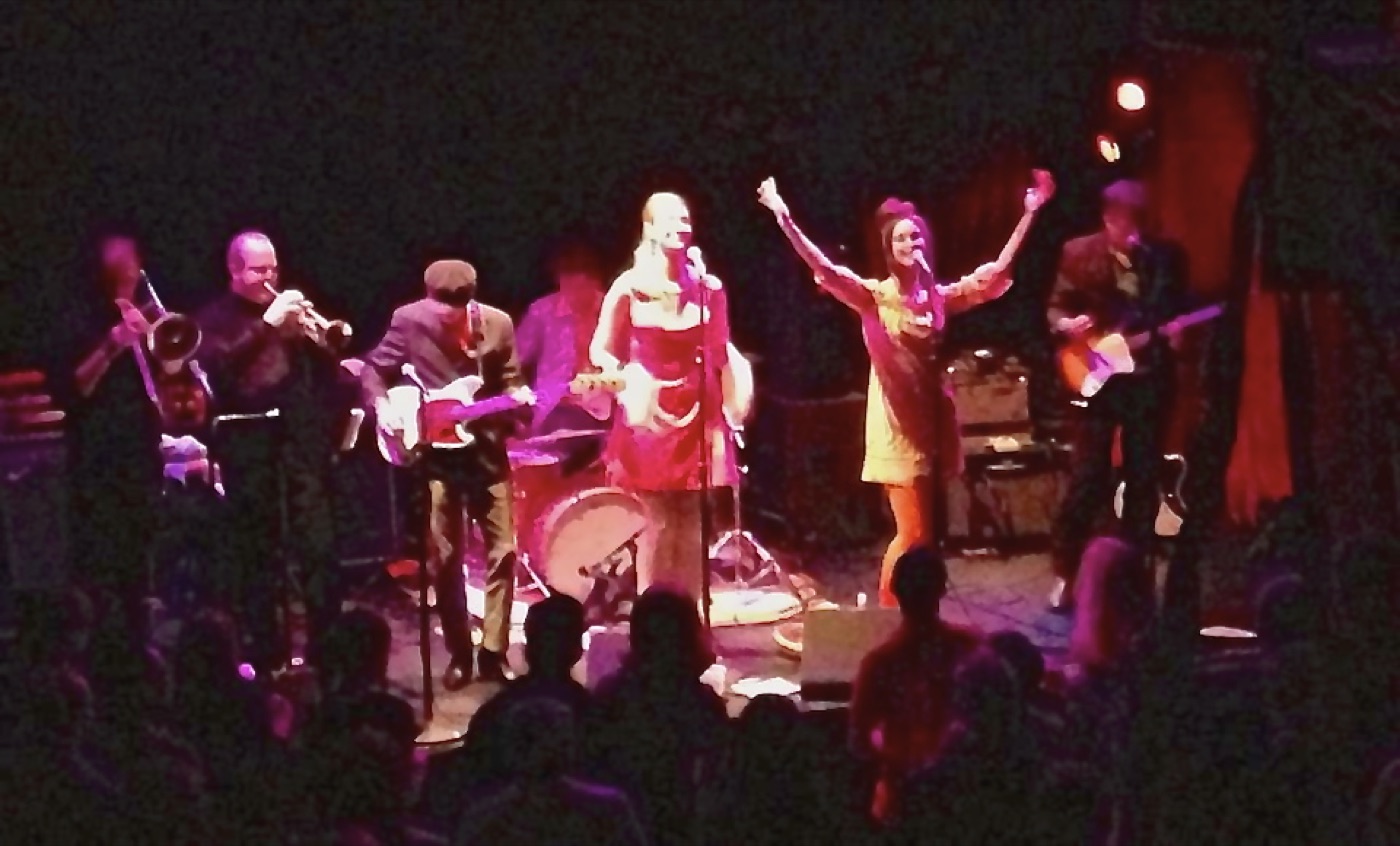 The band onstage from the back of a packed room, arms raised