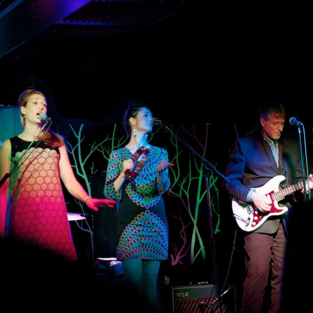 Singers and guitarist onstage beside a Vox amplifier
